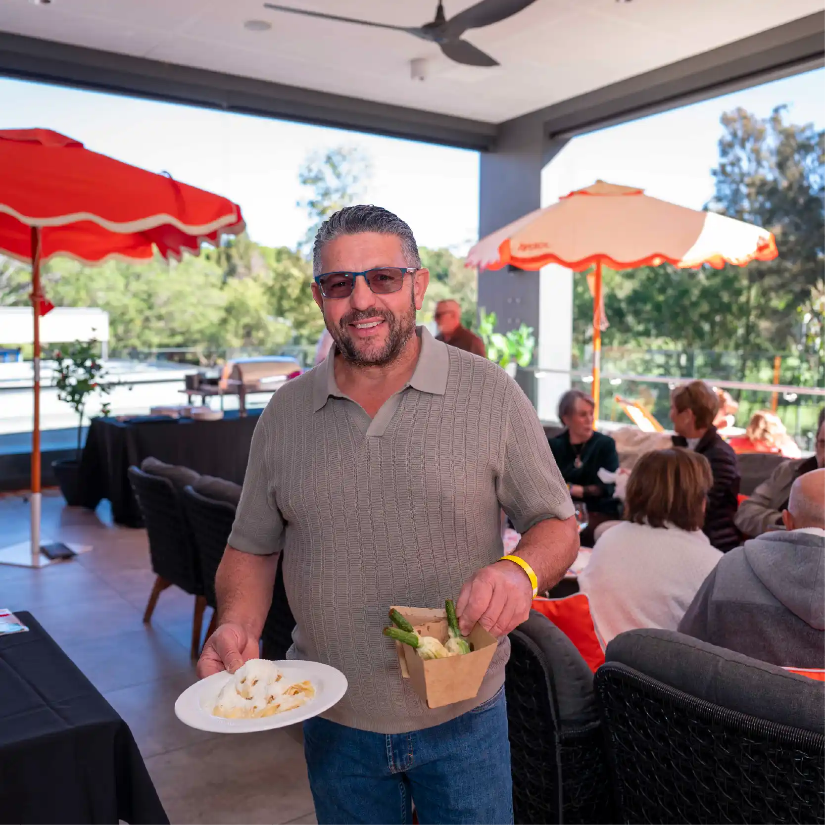 A man wearing sunglasses holding food and beverage smiling.