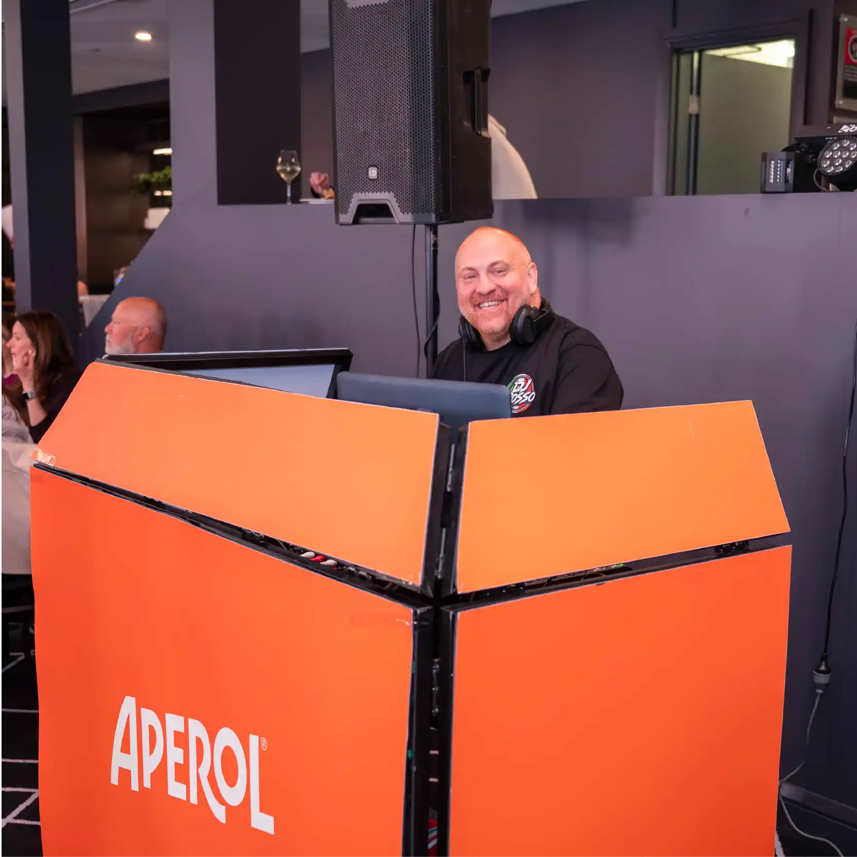 DJ Rosso standing behind the Aperol stand and smiling to the camera